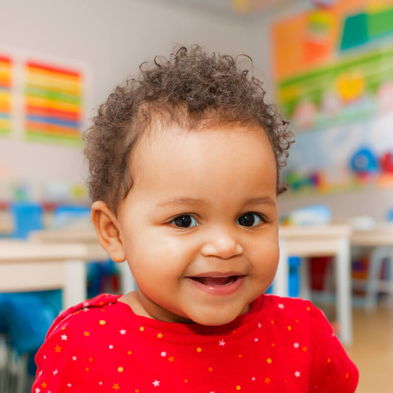 A cheerful baby in a classroom setting, engaging with vibrant learning tools, representing the concept of baby care.