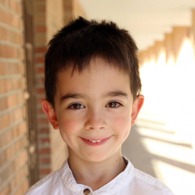 A young boy with black hair dressed in a white shirt, standing with a cheerful expression.