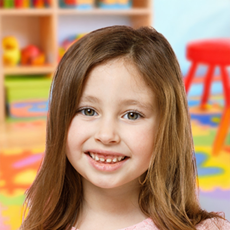 A cheerful young girl smiles widely in a classroom, with vibrant posters and learning tools visible in the background.