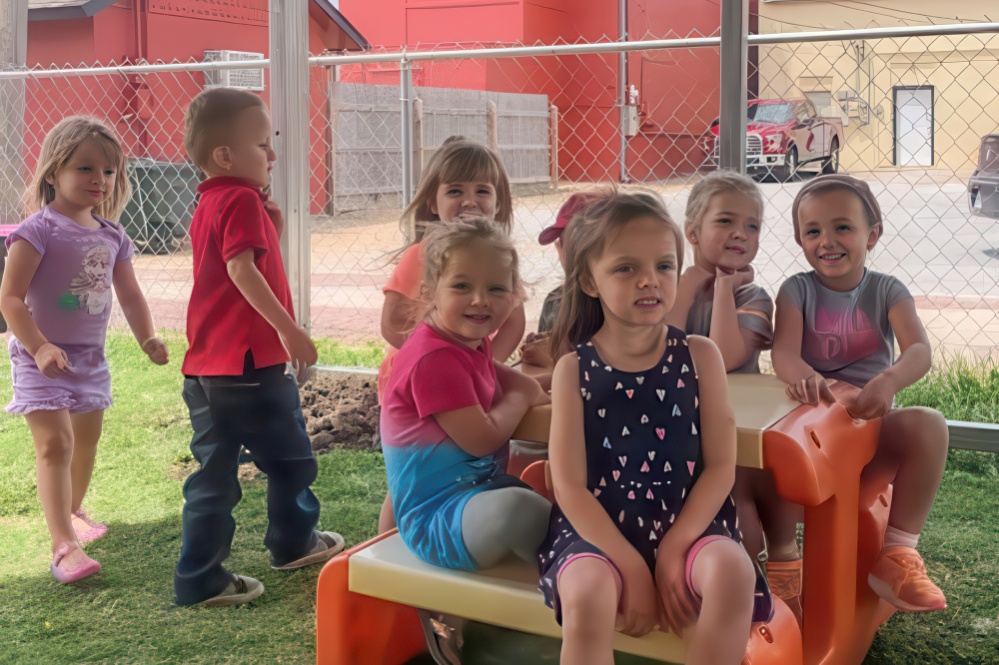 A group of children joyfully sitting on a bench in a yard, enjoying their time outdoors during a big adventure.