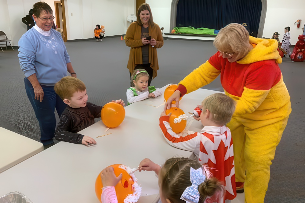 A woman in a colorful costume joyfully holds a balloon, engaging with children in a festive atmosphere.