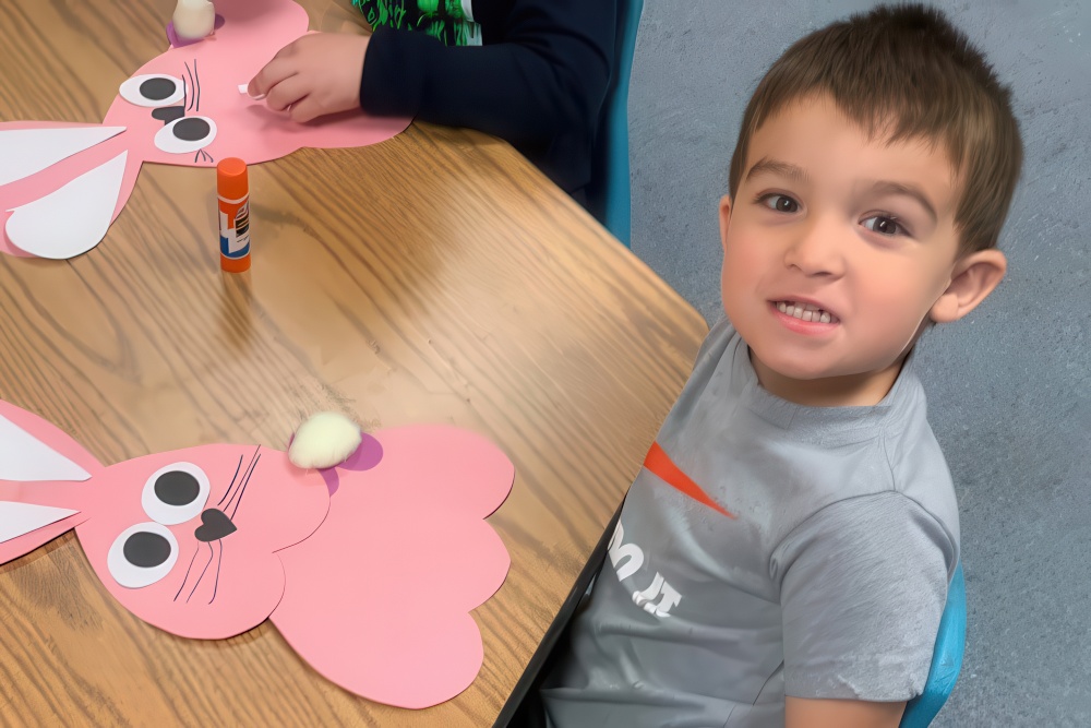 A boy sits at a table, focused on creating a bunny craft, embodying creativity and joy with Brightwheel™ support.