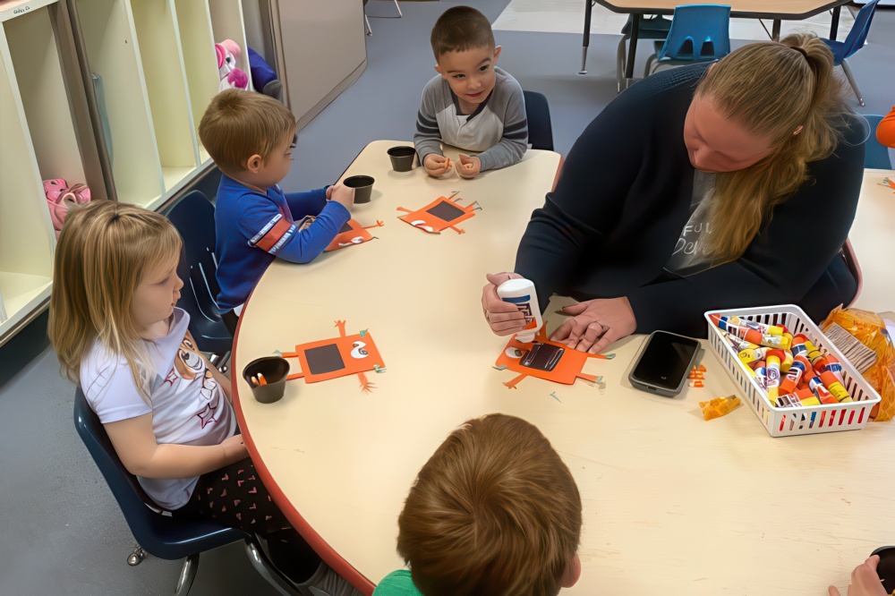 A woman instructs children in a small class on building a robot, fostering creativity and hands-on learning opportunities.