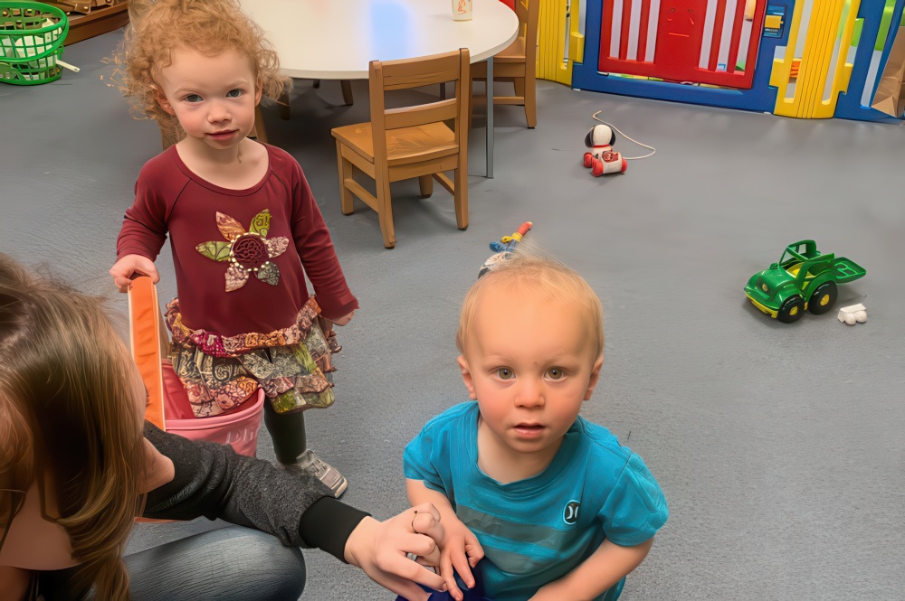 A woman supervises two children playing in a colorful playroom, promoting safety and connection with Brightwheel™.