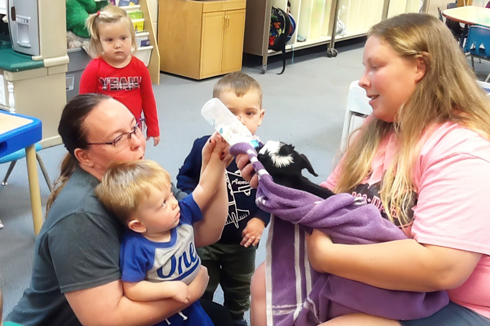 Teacher feeding a baby dog with children, embodying nurturing care and blended curricula for well-rounded development.