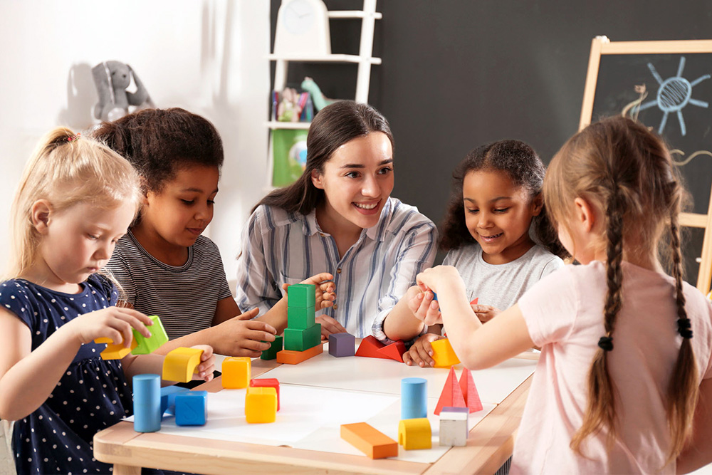 A teacher engages with young students in a hands-on learning activity, fostering creativity and teamwork in the classroom.