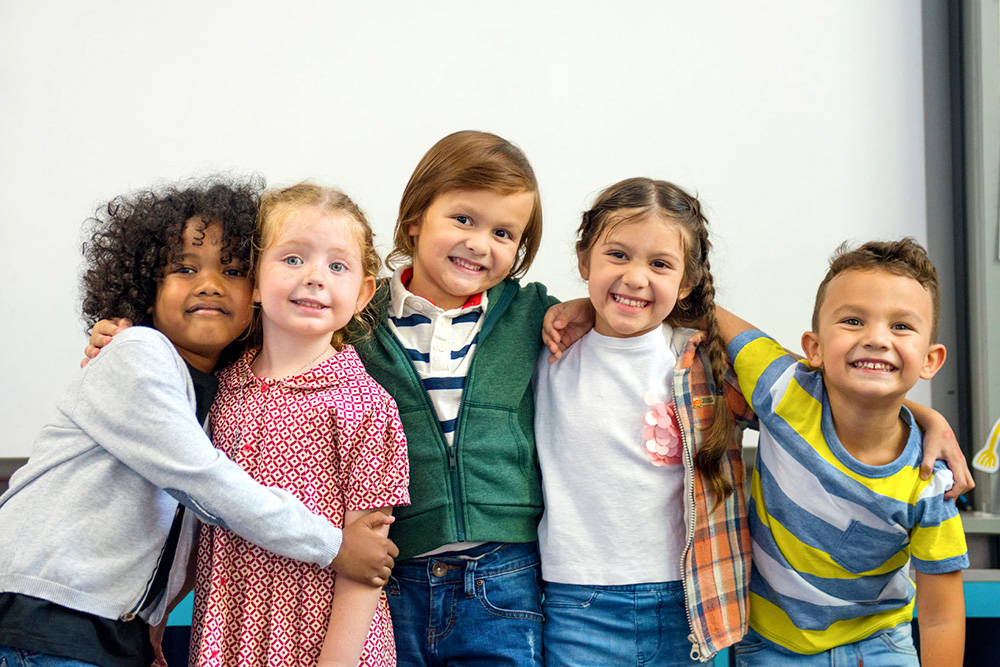 A cheerful group of children poses in front of a wall, their smiles reflecting joy and togetherness.