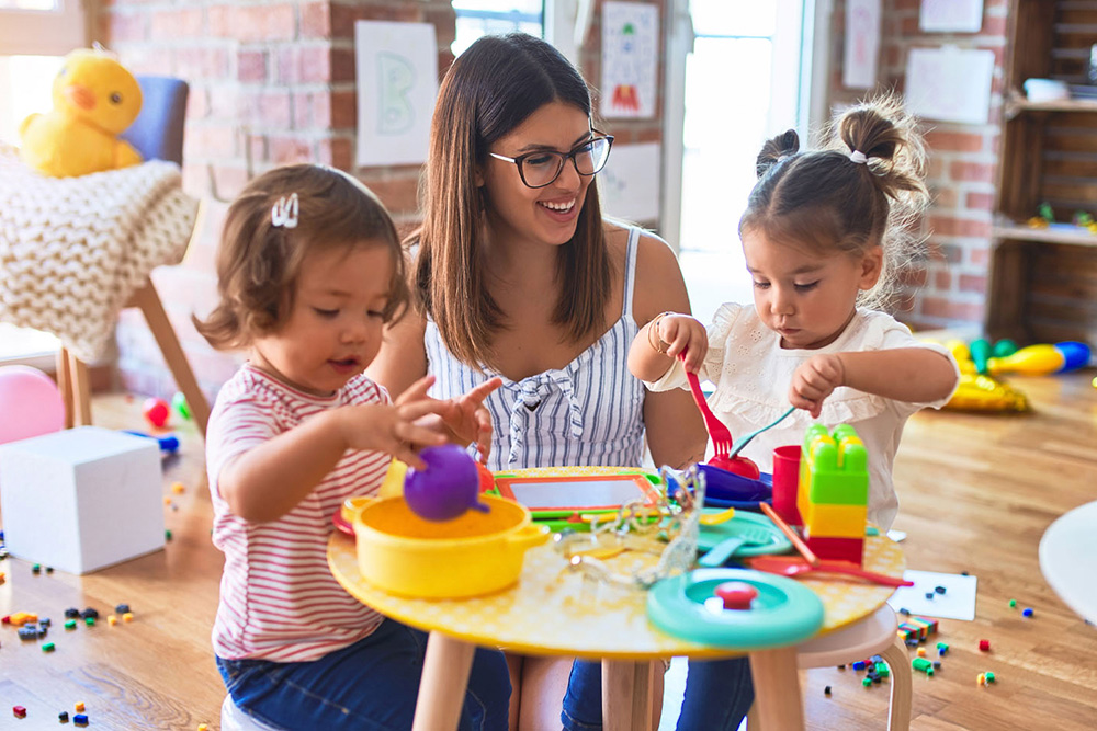 A woman and two children are seated together in a classroom, engaged in a learning activity.