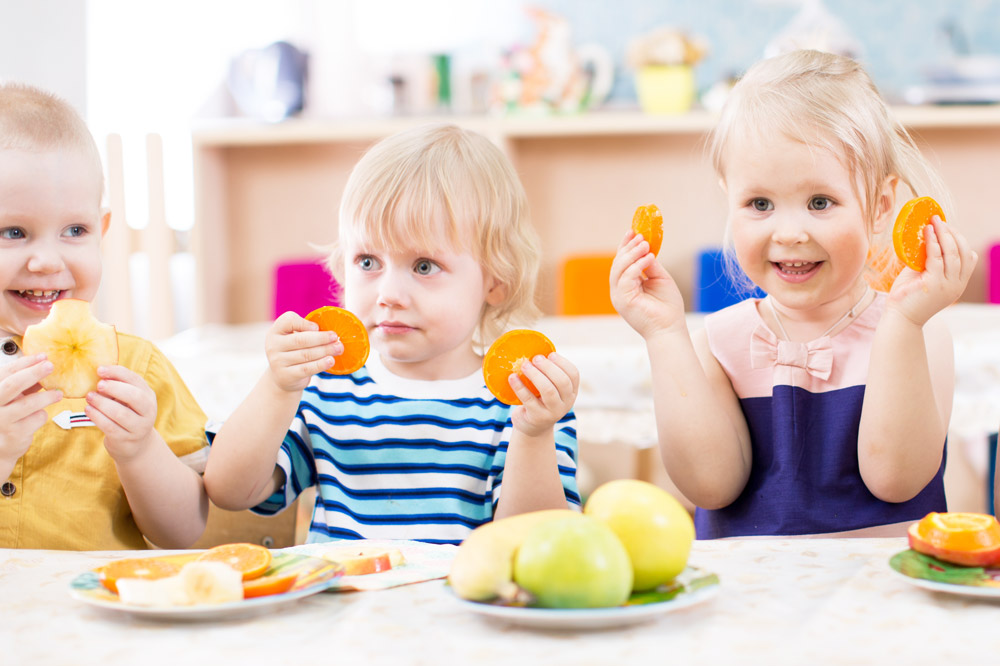 Three children enjoy a variety of fruits at a table, highlighting the benefits of our All-Inclusive Food Program.