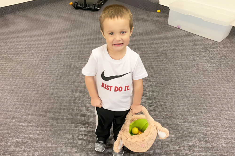 A young boy smiles while holding a stuffed animal in one hand, showcasing joy and innocence.