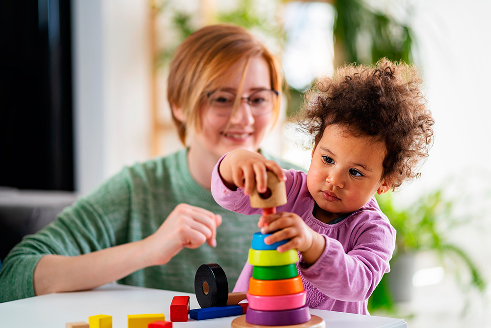 A woman and child joyfully engage with vibrant toys, embodying the principles of a blended curriculum for balanced growth.