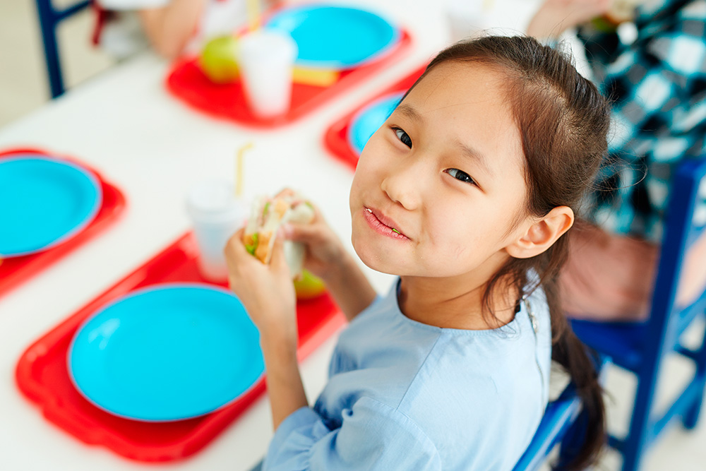 A young girl sits at a table, happily eating a healthy lunch that energizes her for after-school fun.