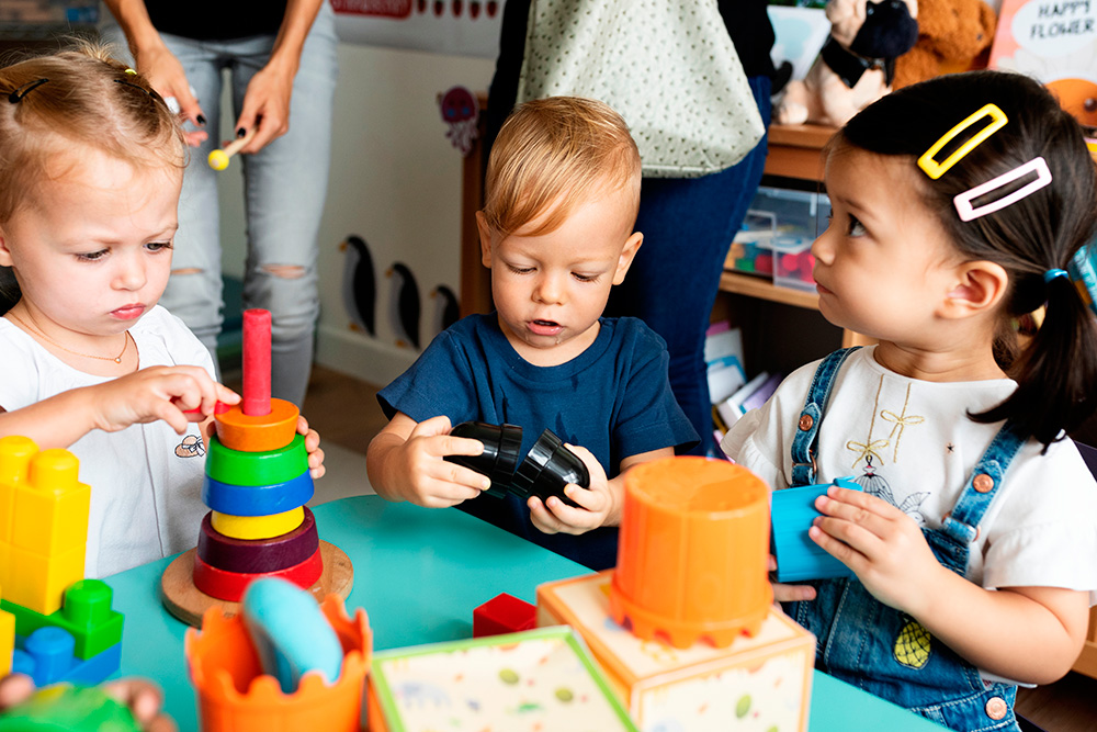 Three children joyfully playing with toys in a vibrant classroom, embodying a nurturing environment for growth.