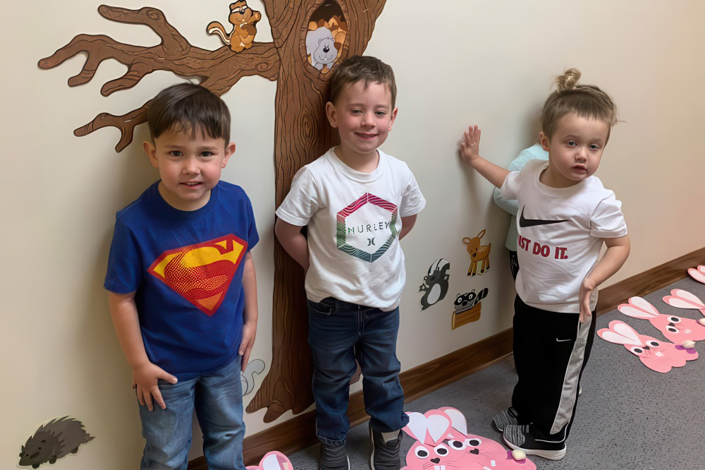 Three children pose in front of a tree mural on a wall, showcasing joy and creativity in their environment.