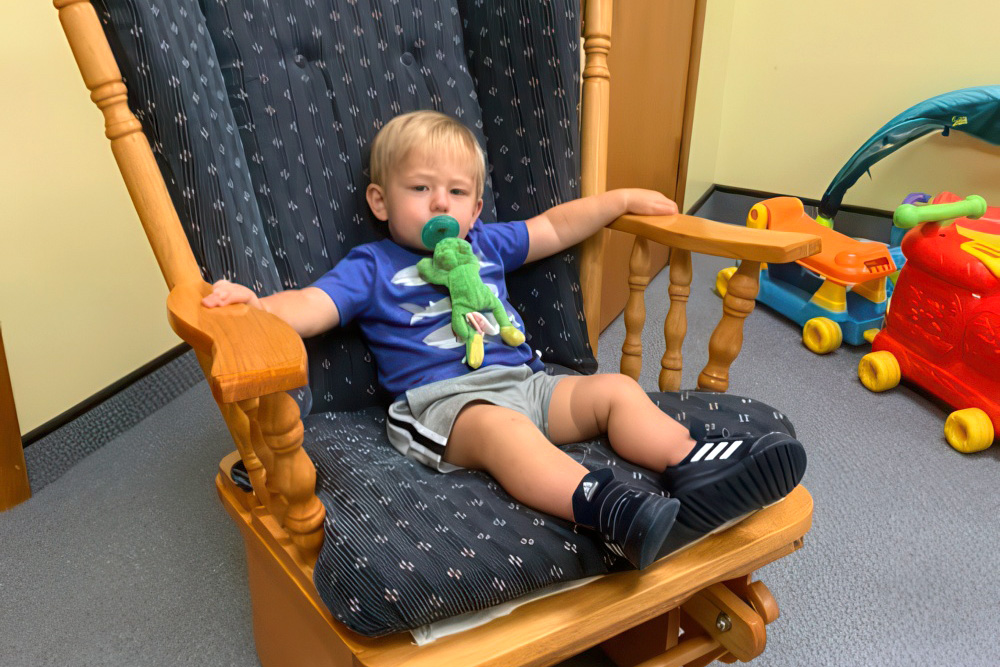 A young child relaxes in a rocking chair, engaged with a toy, representing dependable and affordable childcare.