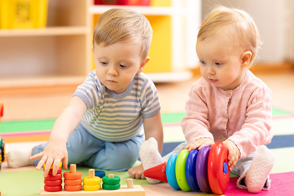 Two young kids playing with colorful toys on the floor, capturing a joyful and playful atmosphere.