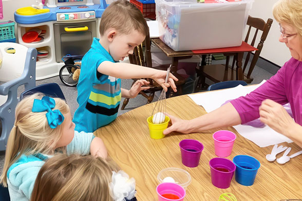 A woman guides children as they participate in various activities, promoting teamwork and creativity.